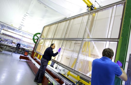 Two men work on an anode plane assembly, which resembles a giant, multi-paned window